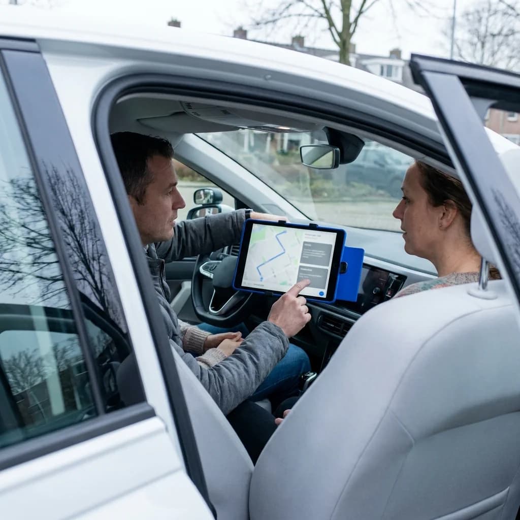 Een rij-instructeur bespreekt de route met een leerling via een app op de tablet in de auto.